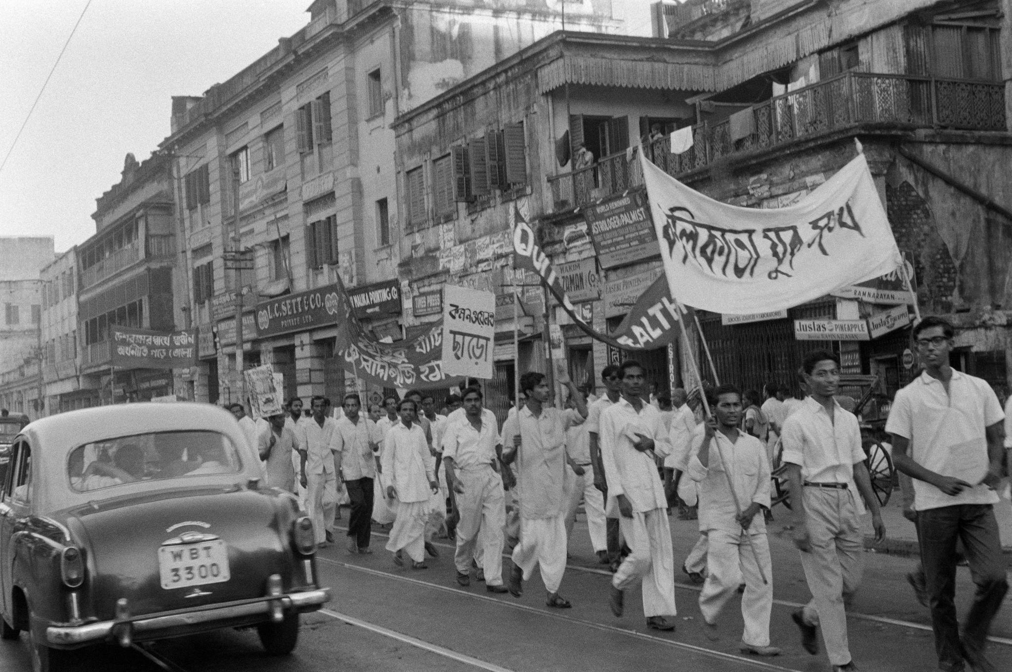 Protesters marching through Kolkata streets holding banners and flags during a political demonstration,
