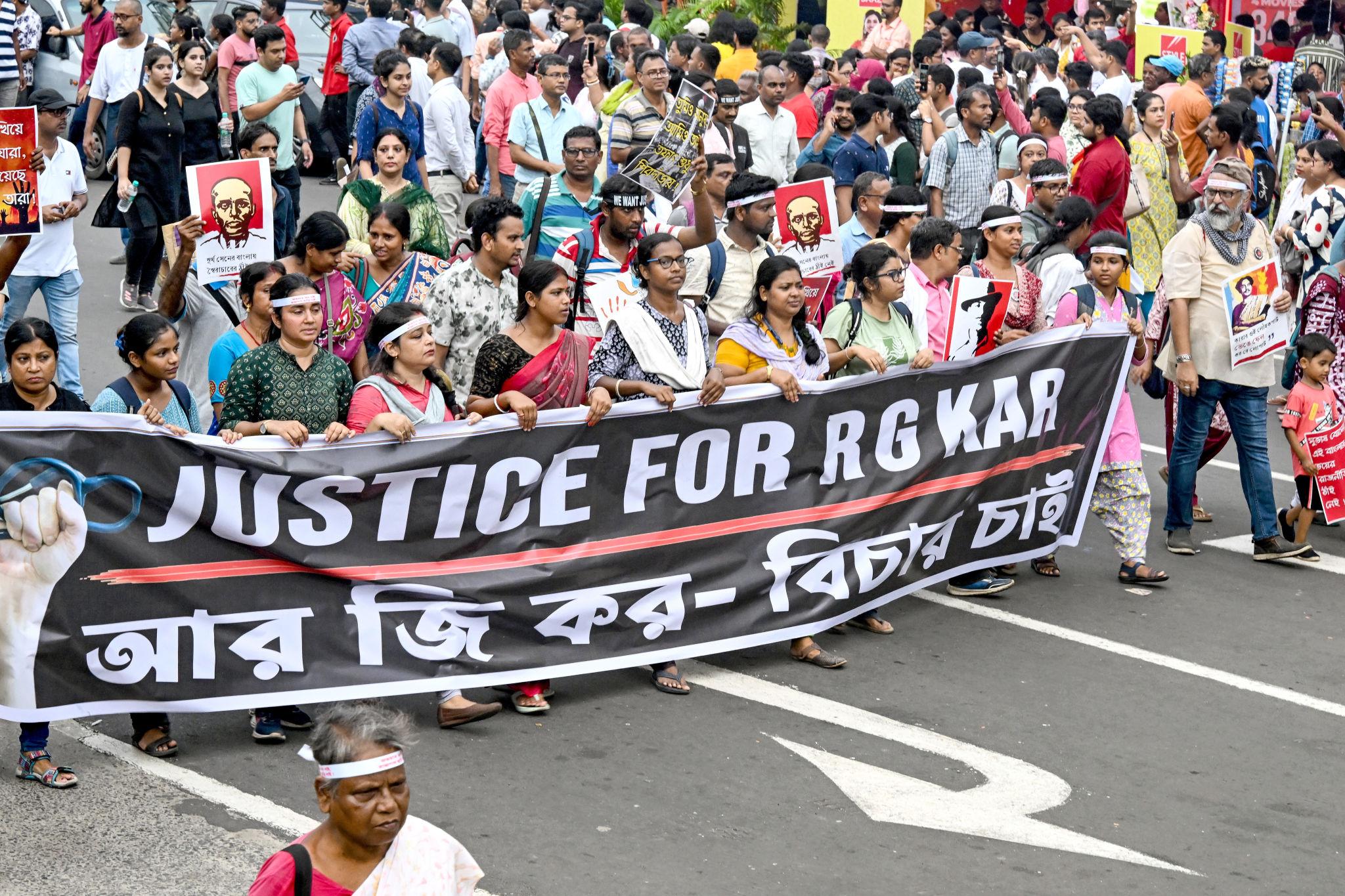 Large crowd marching on the streets holding a banner demanding justice for RG Kar case in Kolkata,